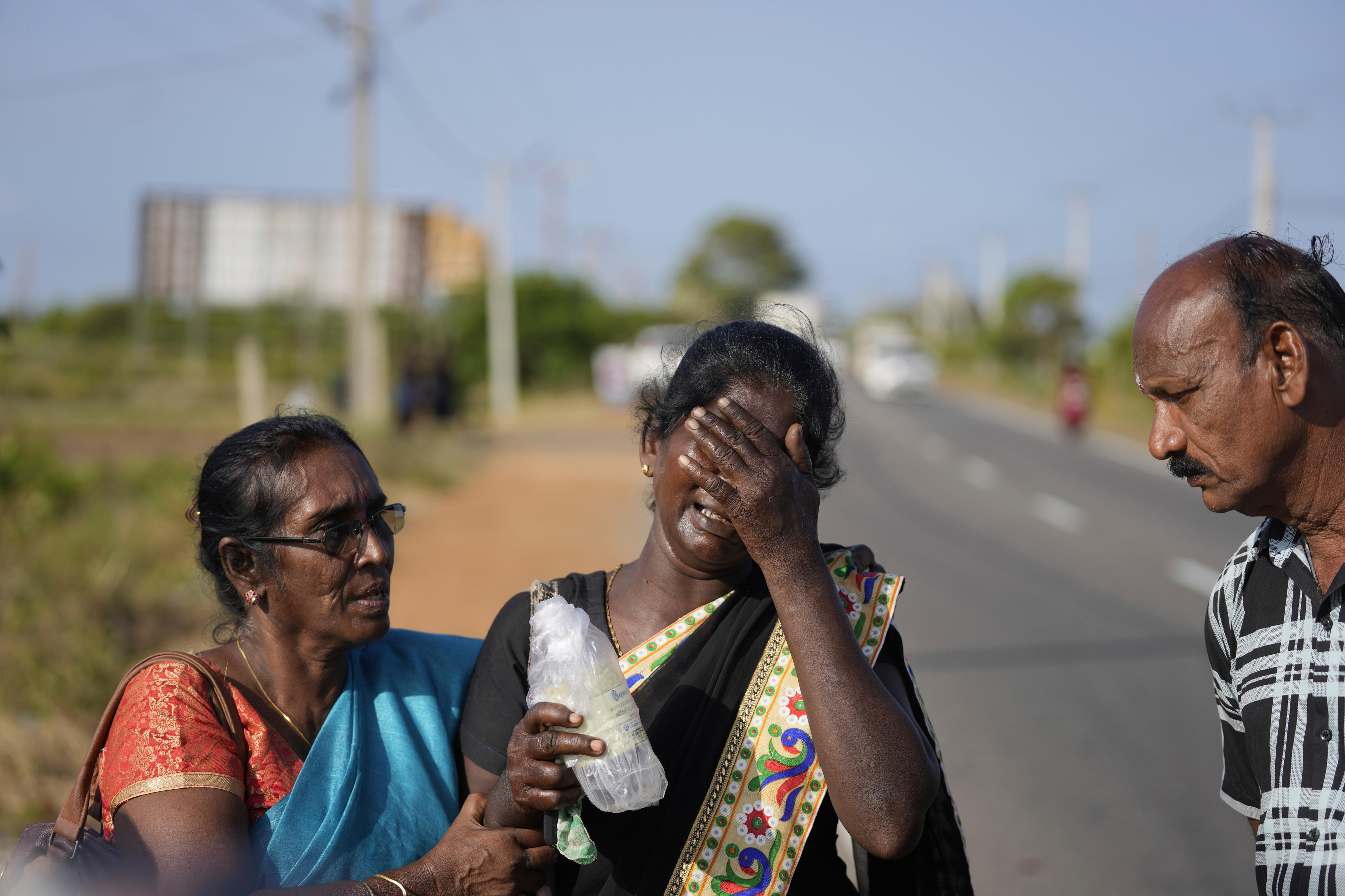 A mother covers her face in grief as a woman beside her tries to comfort her.