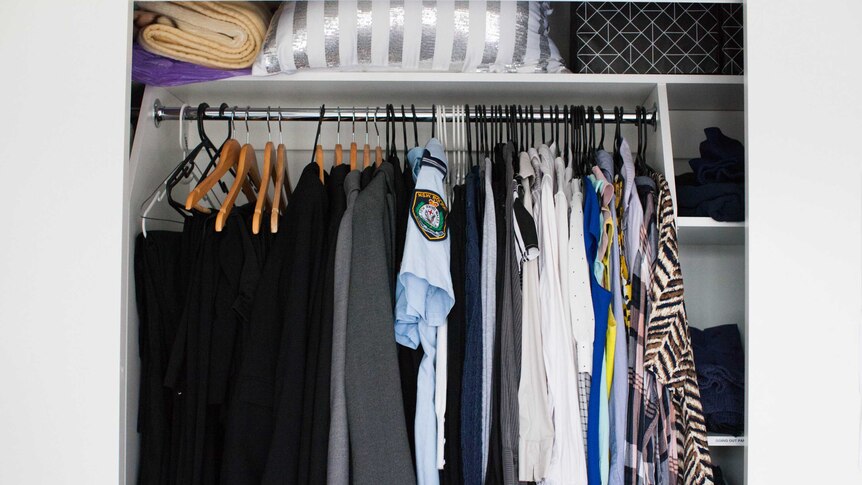 A wardrobe opened to show a collection of shirts, suits and police uniforms