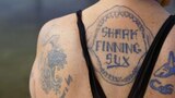 A close up of a woman's back in swimmers with a tattoo that says 'shark finning sux'.