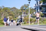 a group of people strolling outdoors in Sydney along a footpath as a woman pushes a pram and a man jogs