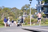 a group of people strolling outdoors in Sydney along a footpath as a woman pushes a pram and a man jogs