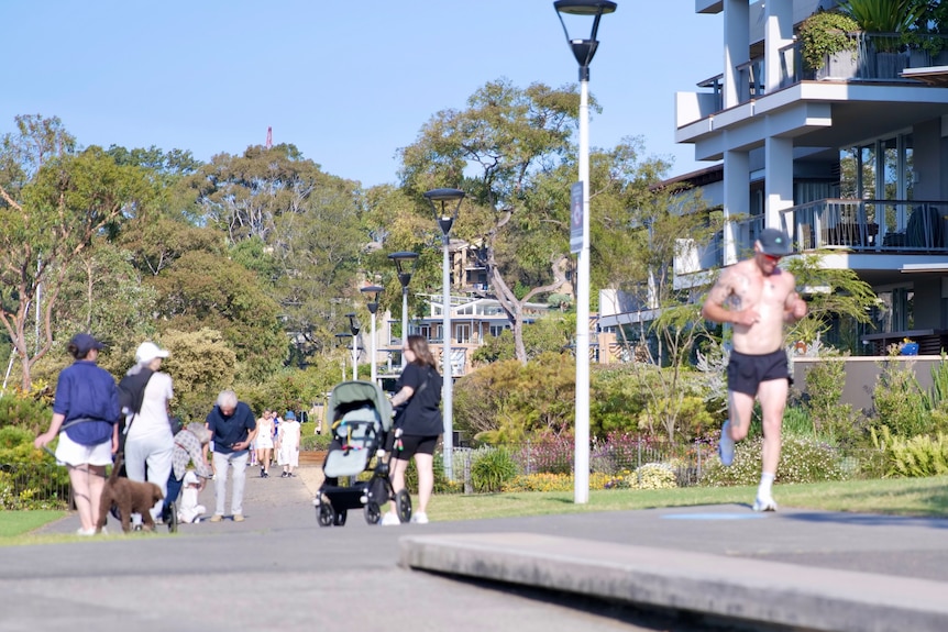 a group of people strolling outdoors in Sydney along a footpath as a woman pushes a pram and a man jogs