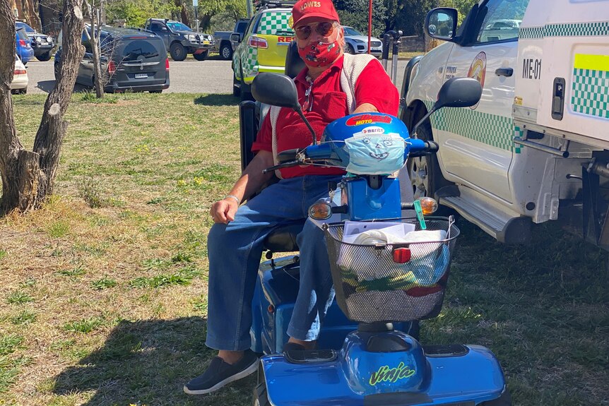 A man sits on a mobility scooter with a face mask taped to the front