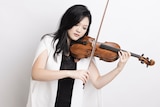 Violinist Emily Sun wearing a white jacket and playing her violin with her eyes closed.
