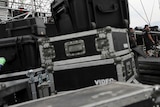 Crates are stacked on top of each other before a concert. Men in the background set up.