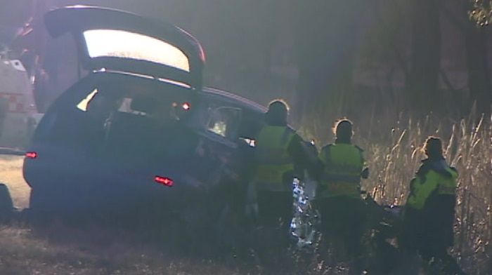 Four police in high-visibility clothing examine the wreck of a car on the side of the road.