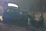 Four police in high-visibility clothing examine the wreck of a car on the side of the road.