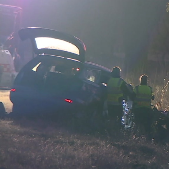 Four police in high-visibility clothing examine the wreck of a car on the side of the road.