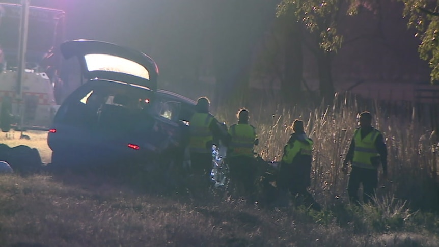 Four police in high-visibility clothing examine the wreck of a car on the side of the road.