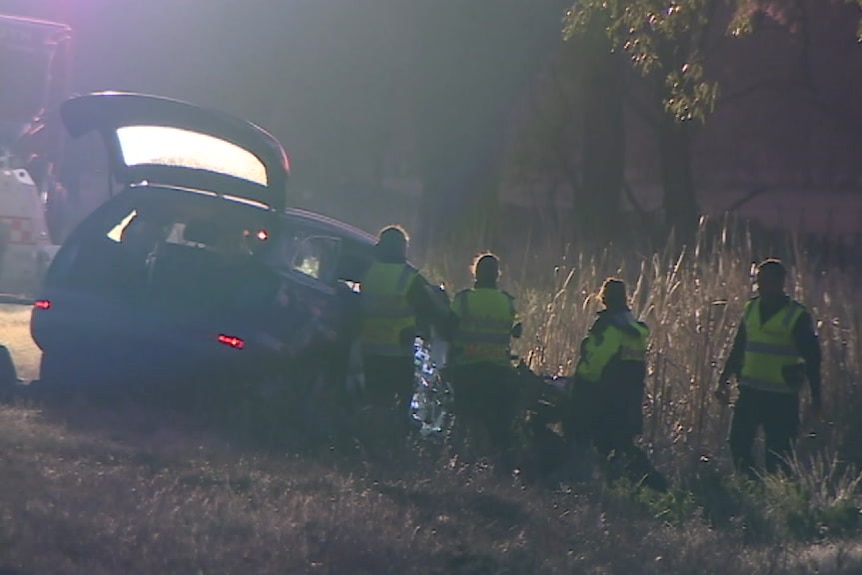 Four police in high-visibility clothing examine the wreck of a car on the side of the road.