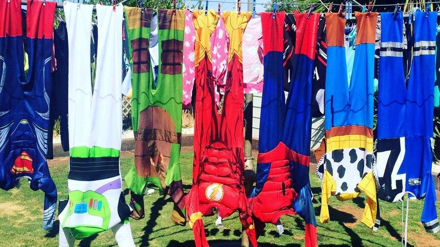 Superhero costumes hang on a clothes line in the back yard of a house.