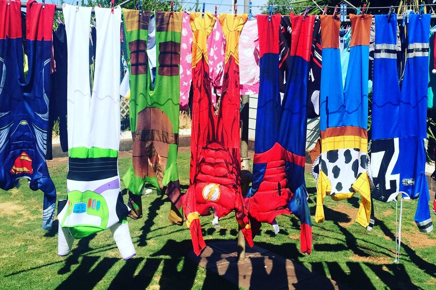 Superhero costumes hang on a clothes line in the back yard of a house.