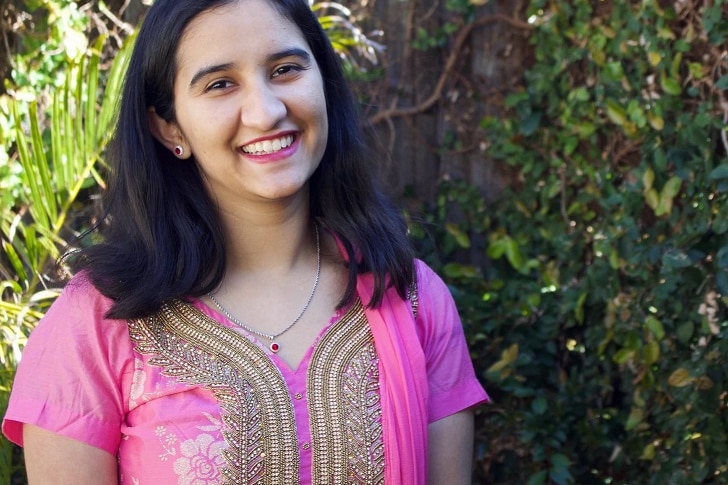 Nandini Sharma, wearing a pink blouse and necklace, stands in a garden.