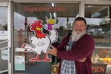 A bearded man smiles outside the window of a chicken shop.
