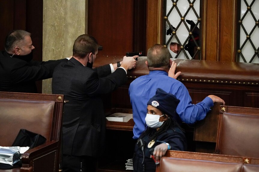 Security officers draw their guns as rioters try to break into the US house of representatives.