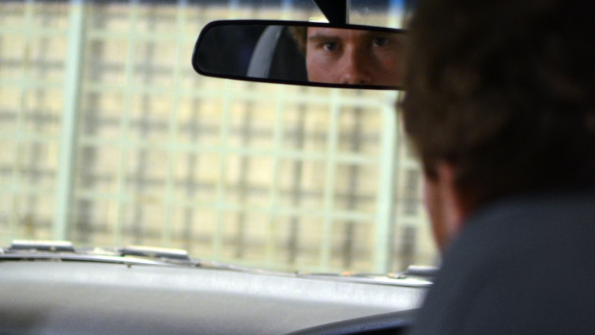 A man looks at the rear view-mirror of a car.