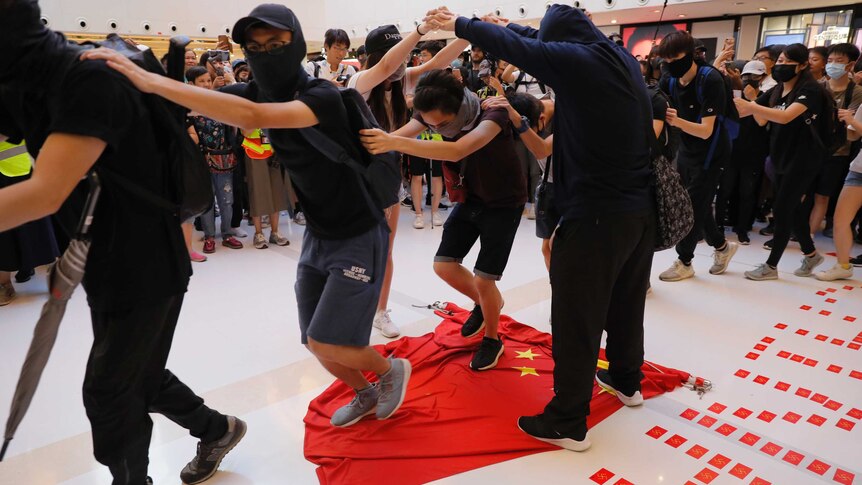 Protesters step on a Chinese flag at a mall in Hong Kong. They have their hands on each others shoulders, and walk in a line.