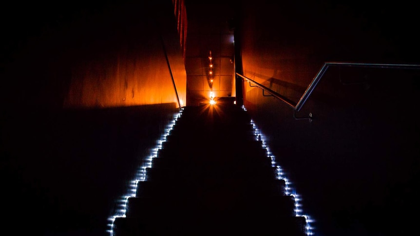 A dimly lit stairwell leads up to a warmly glowing room.