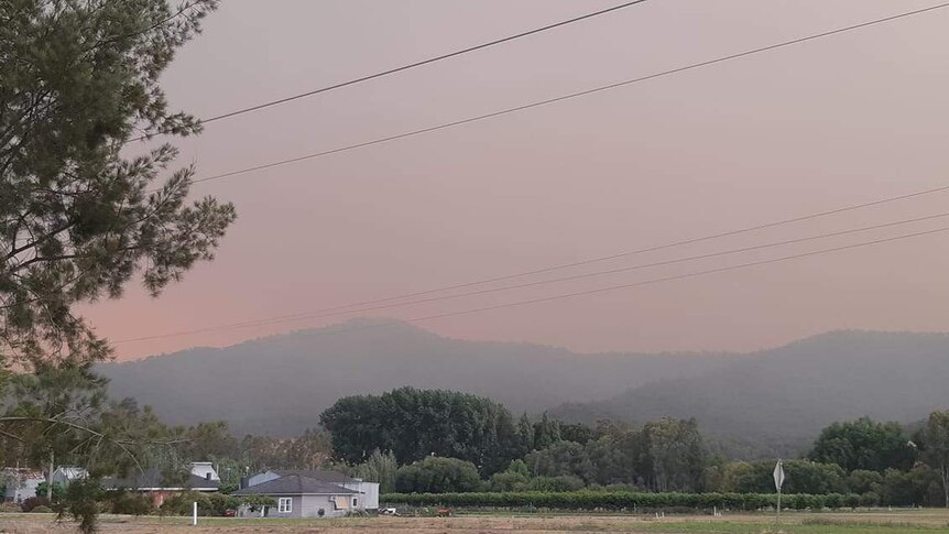 A red glow from fire seen in the distance over hills with smoke shrouding the sky.