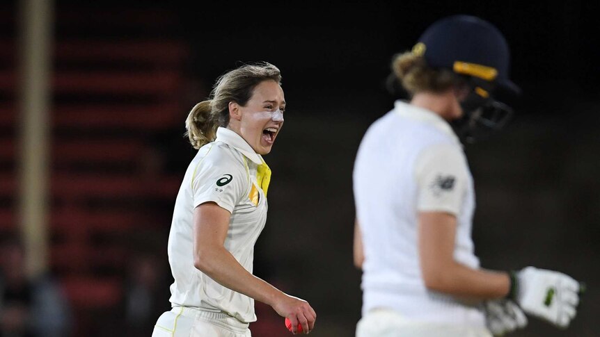 Ellyse Perry smiles in the back ground as a blurred English batter drops her head in the foreground.
