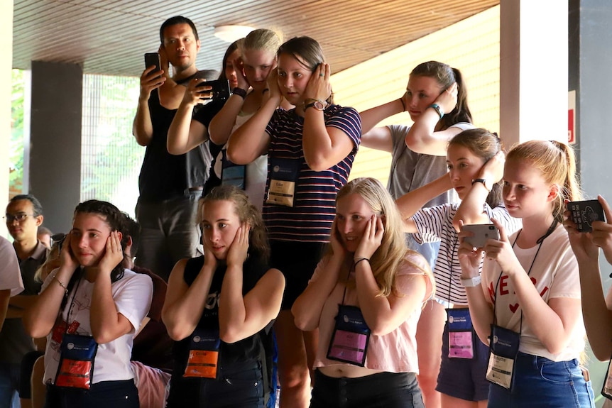 Young women cover their ears.