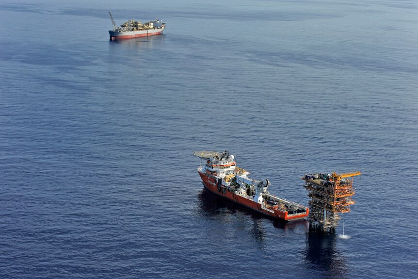 A wide shot of an oil field in the middle of the sea. A ship is parked alongside a rig. 
