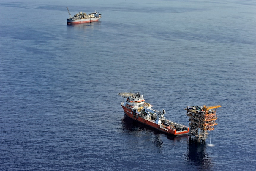 A wide shot of an oil field in the middle of the sea. A ship is parked alongside a rig. 