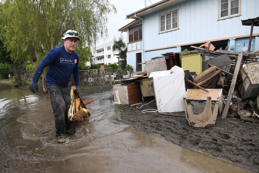 Chris Mitchell walks in muddy water to add flood-damaged items to a pile outside a house in Rosslea in Townsville.