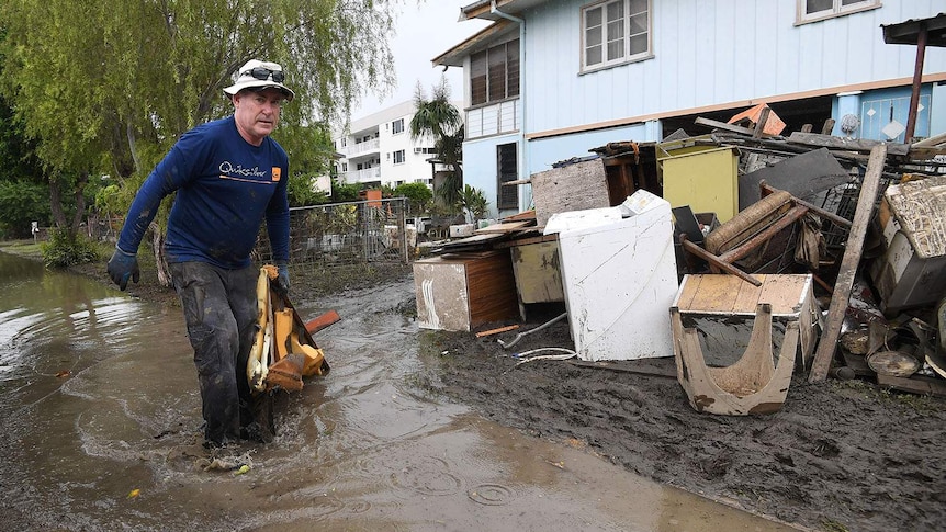 Chris Mitchell walks in muddy water to add flood-damaged items to a pile outside a house in Rosslea in Townsville.