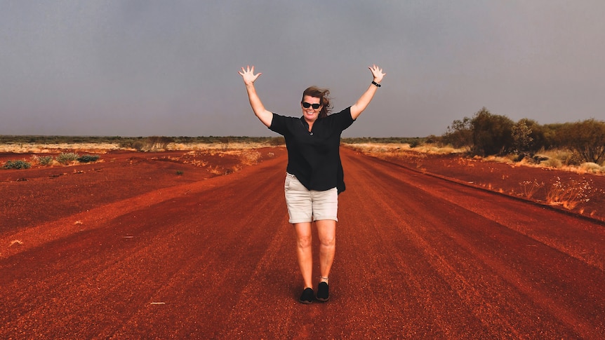 Storm clouds are behind Kylie as she walks on a dirt road with her arms raised