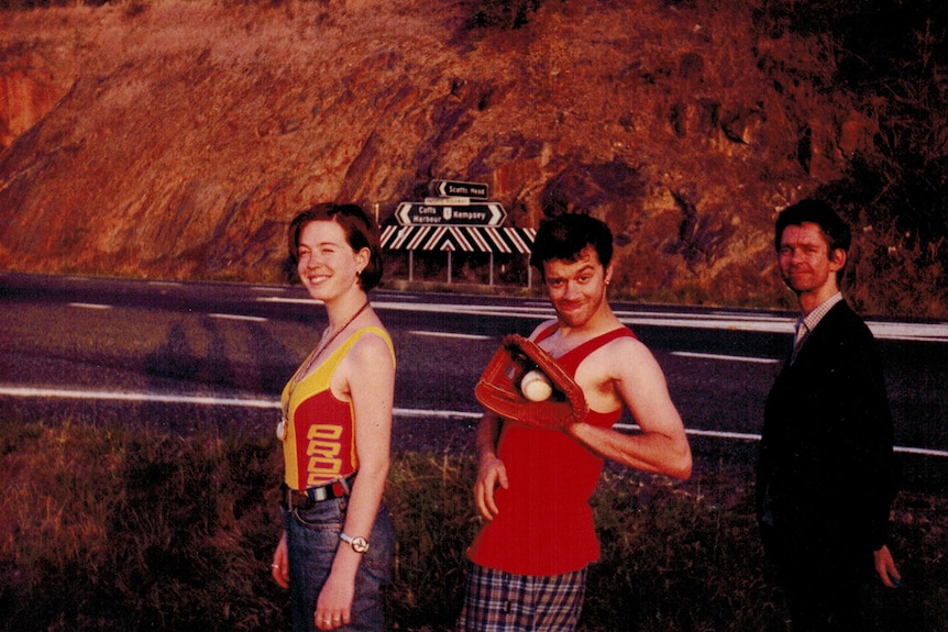 Three members of Frente on the side of a highway between Coffs Harbour and Kempsey. One member has a baseball and mit.