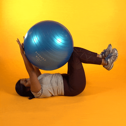 A young woman is lying on her back with a large exercise held above her by her out-stretched arms and knees.