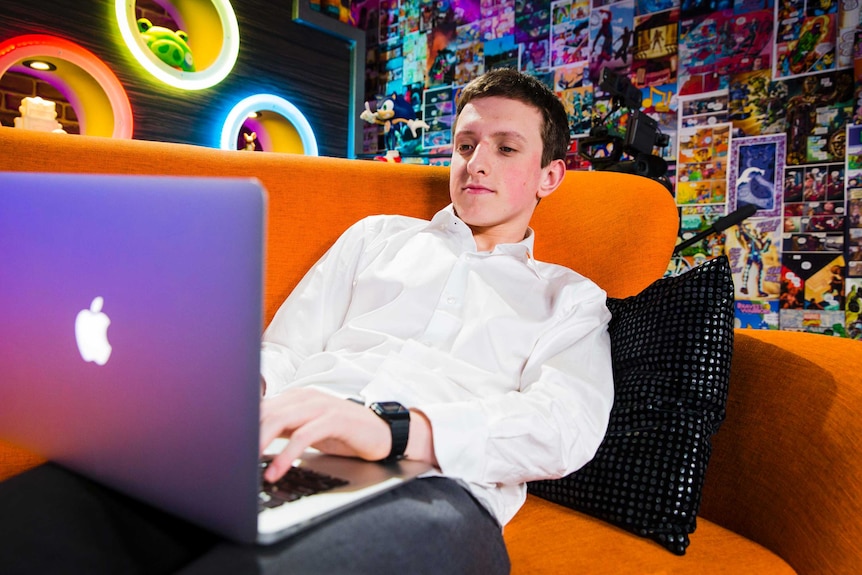 A young man sitting behind a laptop computer.