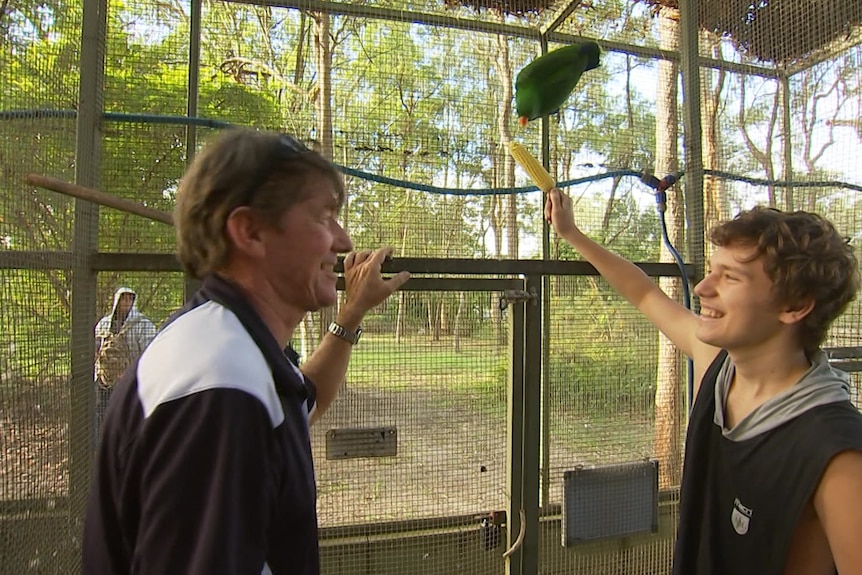 Year 11 student Lachlan with teacher Tim Victory facing each other in an aviary as Lachlan feeds corn to a bird on fence behind 