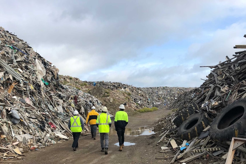 Council inspectors in hi-vis walk between towering piles of construction waste.