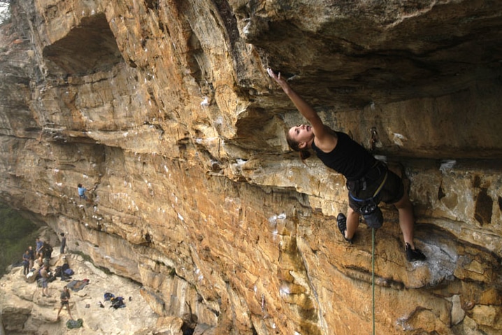Libby Hall climbing a large rock high above the ground.