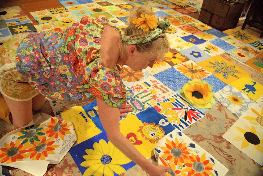 A woman, wearing brightly colour clothes, inspects large sunflower quilt squares.