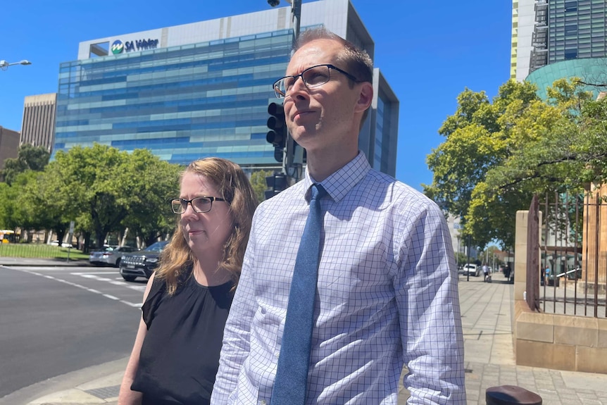 Man wearing shirt, tie, and glasses stands next to woman in front of court.