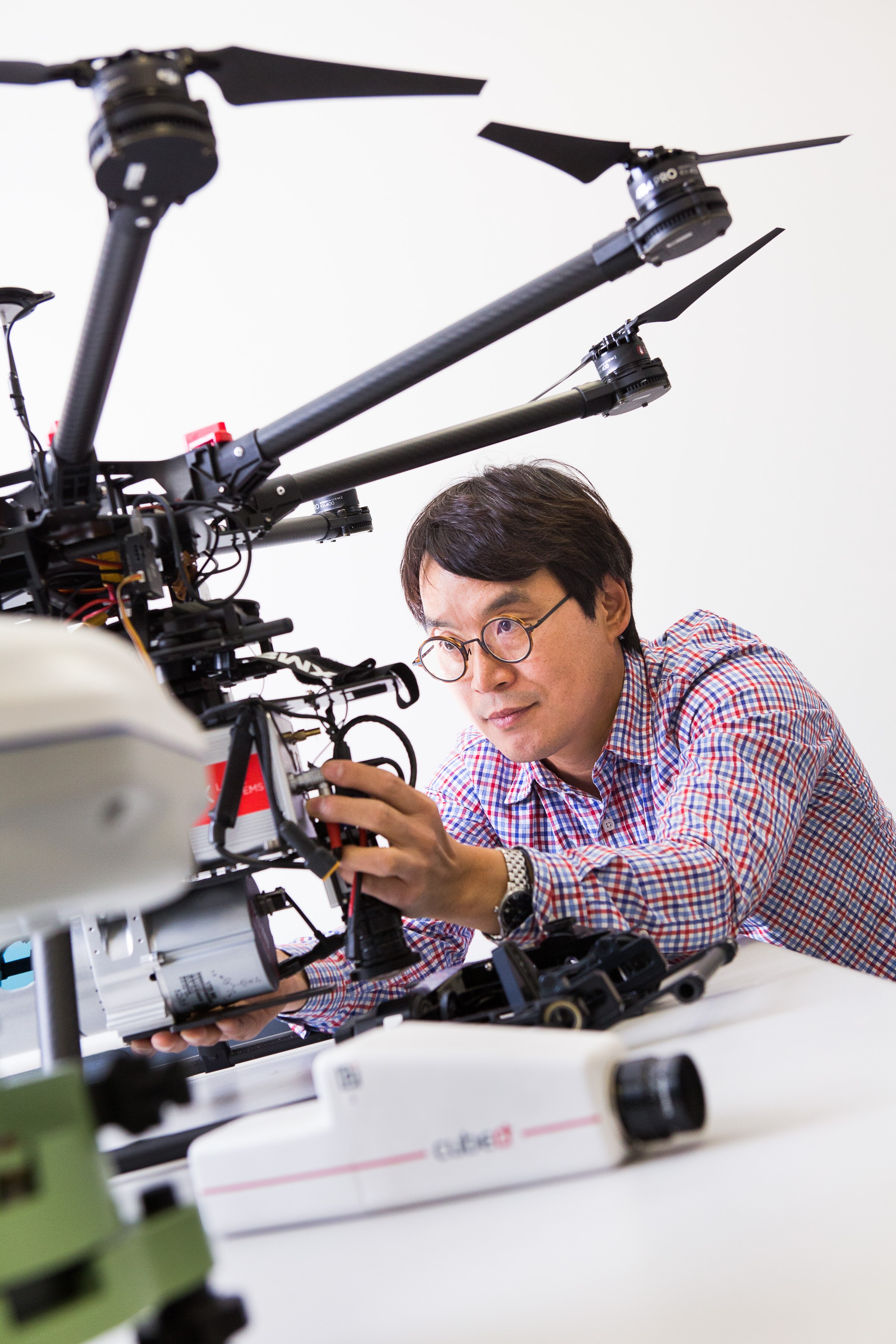 A man with round glasses and a checked shirt checking a large drone at a desk.