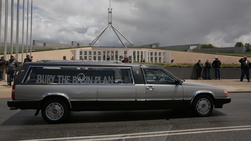 a hearse with a sign inside reading can the plan parks in front of parliament house in Canberra