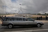 a hearse with a sign inside reading can the plan parks in front of parliament house in Canberra
