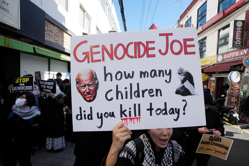 A protester holds a sign saying 'Genocide Joe how many children did you kill today?'