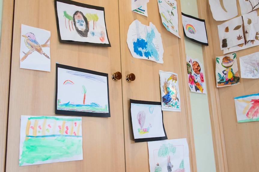Dozens of children's artworks are displayed on a wall in a family home.