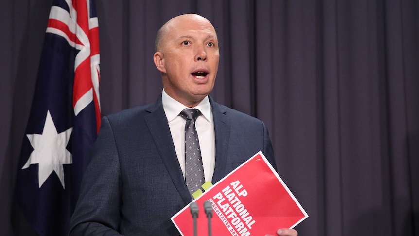 Home Affairs Minister Peter Dutton holds a Labor party document while talking to the media