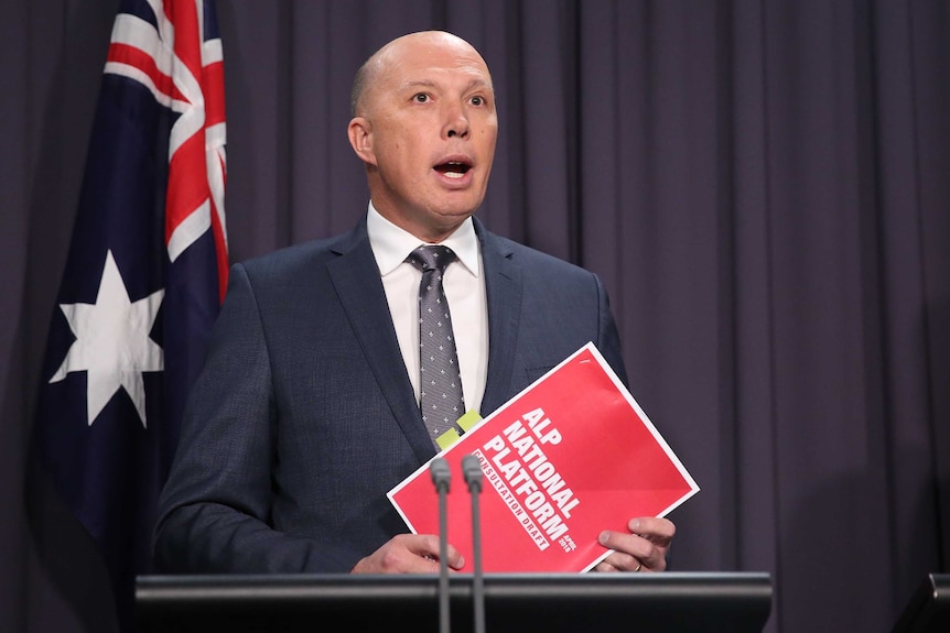 Home Affairs Minister Peter Dutton holds a Labor party document while talking to the media