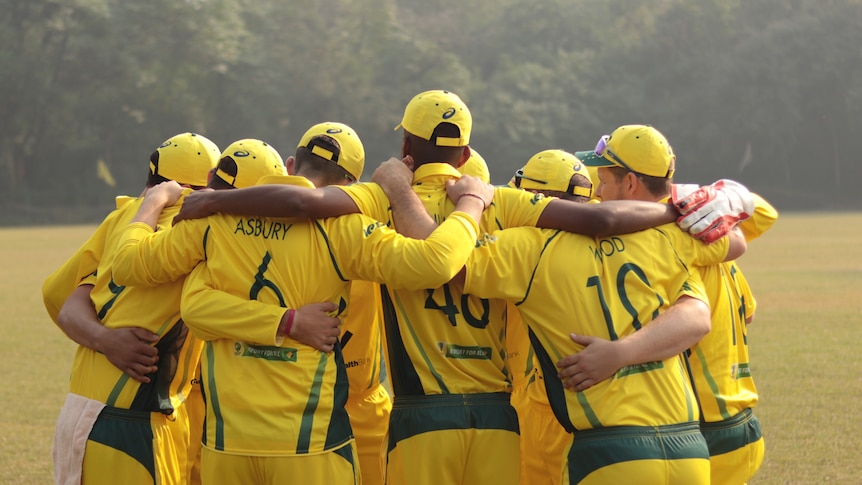 A group of men stand in a huddle wearing yellow cricket kit