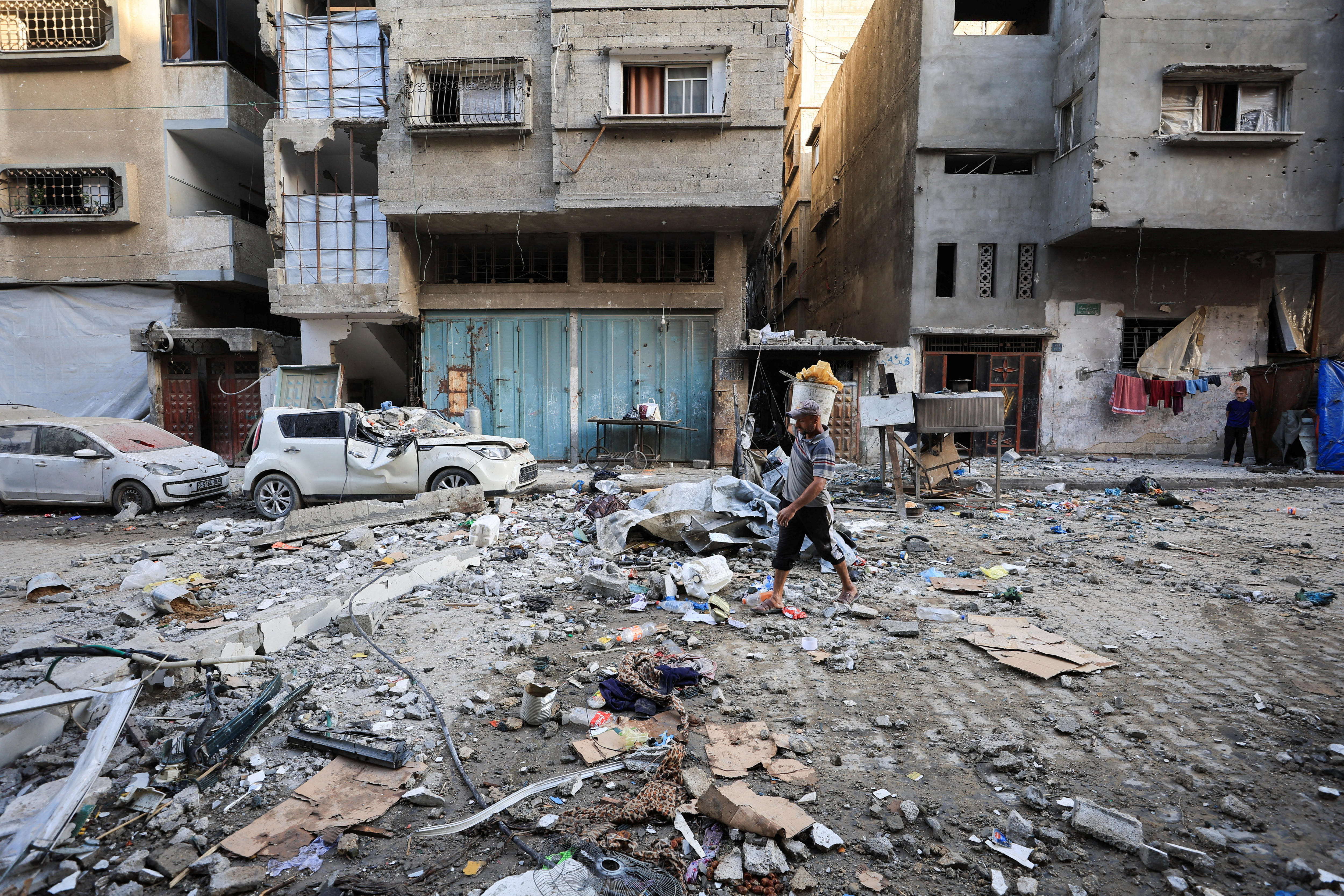 Rubble and destroyed buildings with a man walking on a road alongside squashed cars