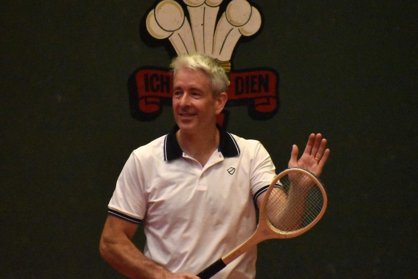 A man in white poses with a racquet