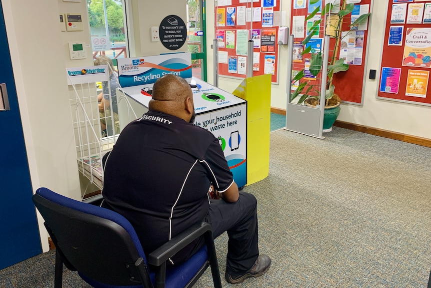 A man in a dark-coloured security shirt sits inside a building