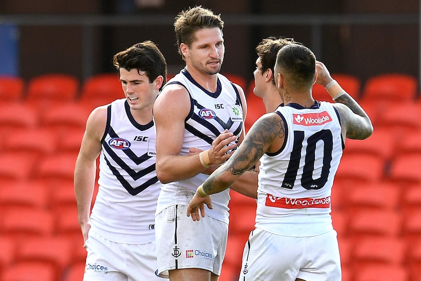 Four Fremantle AFL players group together to celebrate a goal being kicked against North Melbourne.